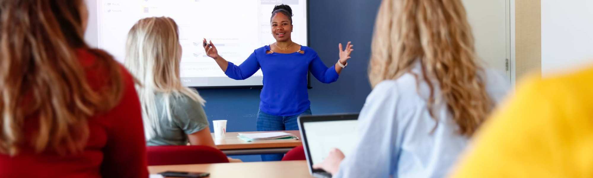 HBO master studenten geven een presentatie bij het scherm voor in de klas, andere studenten luisteren