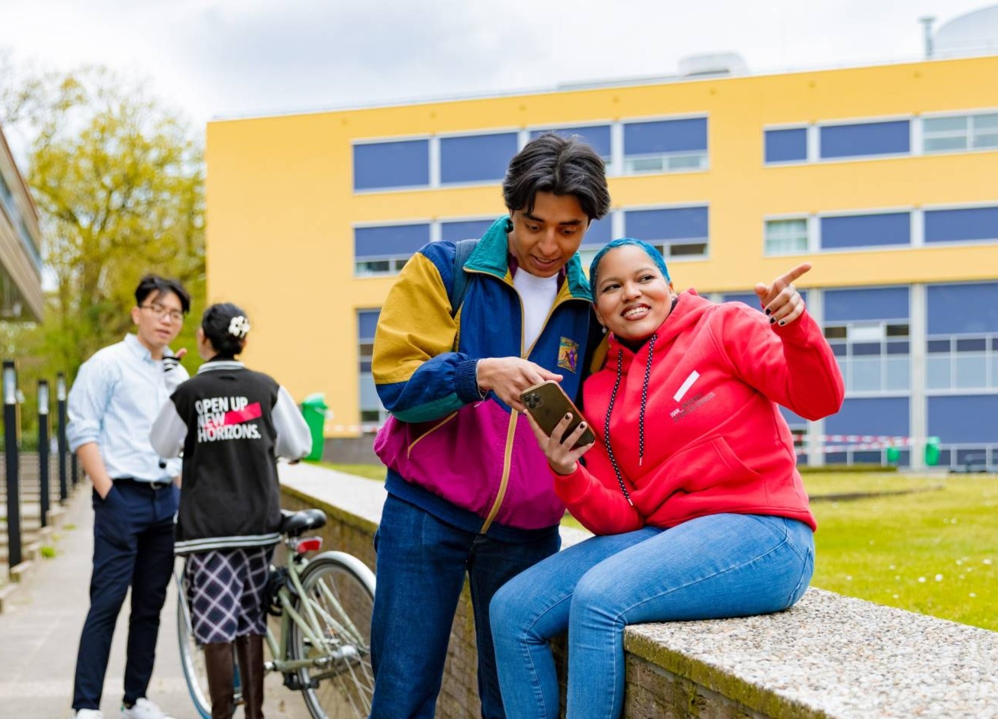 Chadionne pointing at something, Diego pointing at something on a smartphone and two other students by the bicycle in the background at Arnhem Campus.