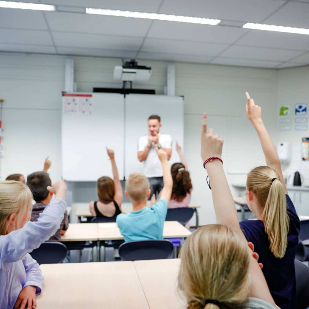 Meester geeft les, kinderen vinger omhoog