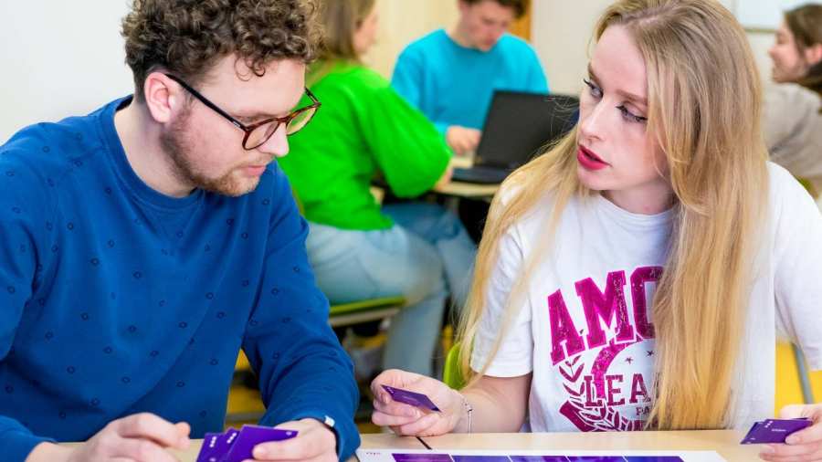 Twee studenten spelen een kaartspel met blauwe kaartjes in een gekleurd leraar Duits lokaal.
