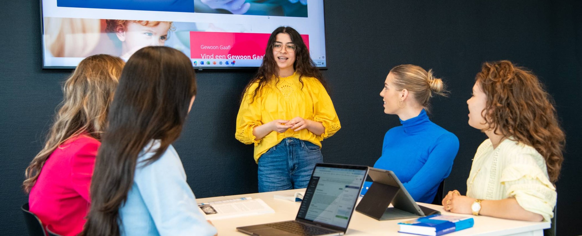 Student staat voor een groep van 4 studenten en geeft met behulp van het digiboard een presentatie.