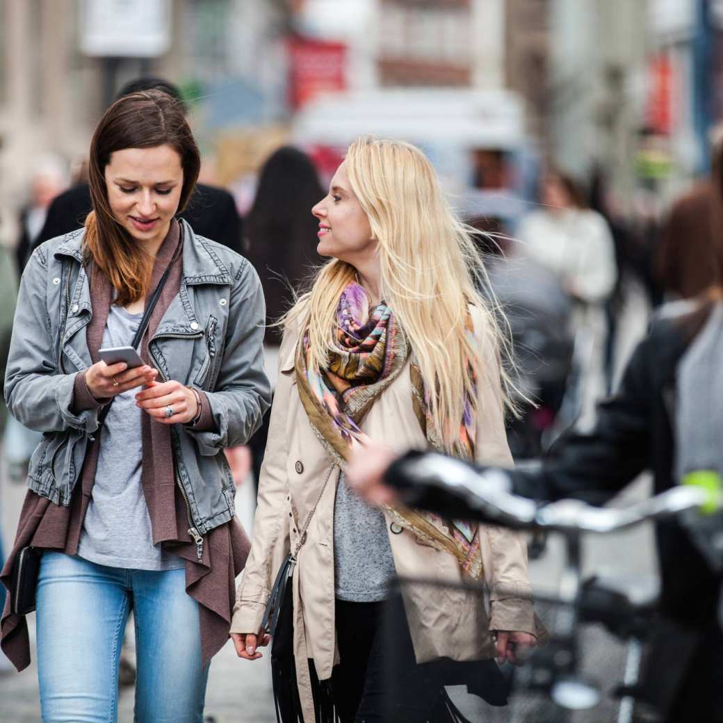 vrouwen lopend door de stad, eentje met fiets, eentje met mobiel