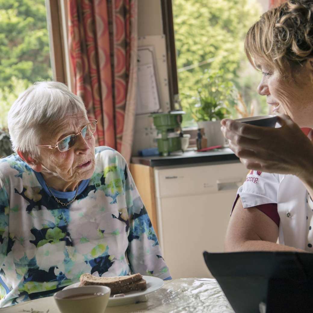 een thuiszorgverpleegkundige helpt een nog thuiswonende oudere dame met beginnende dementie bij de dagelijkse zorgtaken