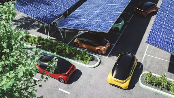 Een rode, gele, groene en oranje elektrische auto op een parkeerterrein met zonnepanelen op het dak. Stockfoto.