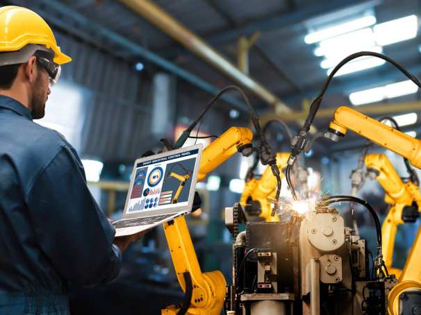 Man met tablet kijkt naar robotarmen in Digitale Fabriek