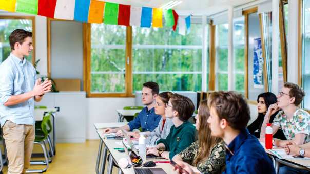 Jonge docent staat voor de klas en geeft les aan zijn groep studenten die aandachtig luisteren naar hem. 