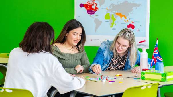 Drie studenten spelen in een lokaal waar de Engelse vlag hangt 'Mens, erger je niet!'
