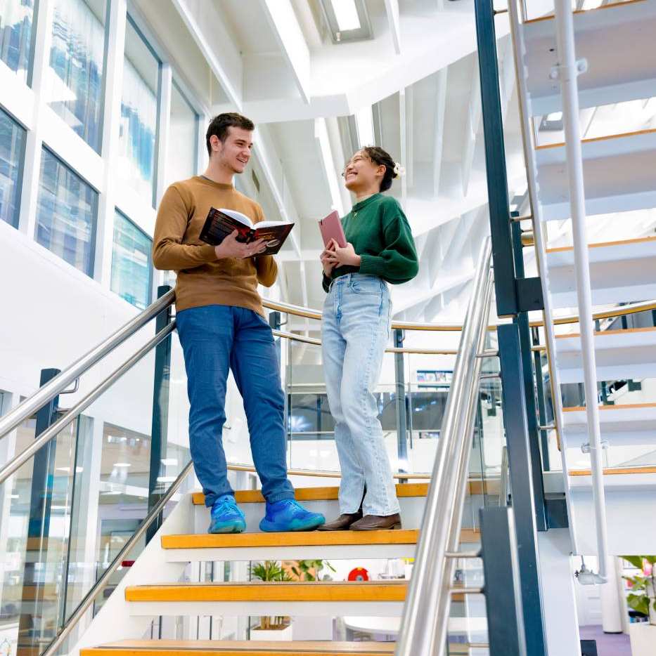 International students Tam and Andrei discussing a book in the library at the Arnhem campus of HAN University of Applied Sciences.