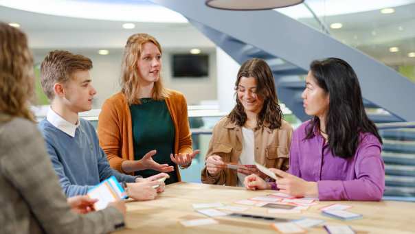 Toegepaste Psychologie TP, foto 2432, studenten doen kaartspel aan tafel en docent geeft uitleg, overleg, samenwerken