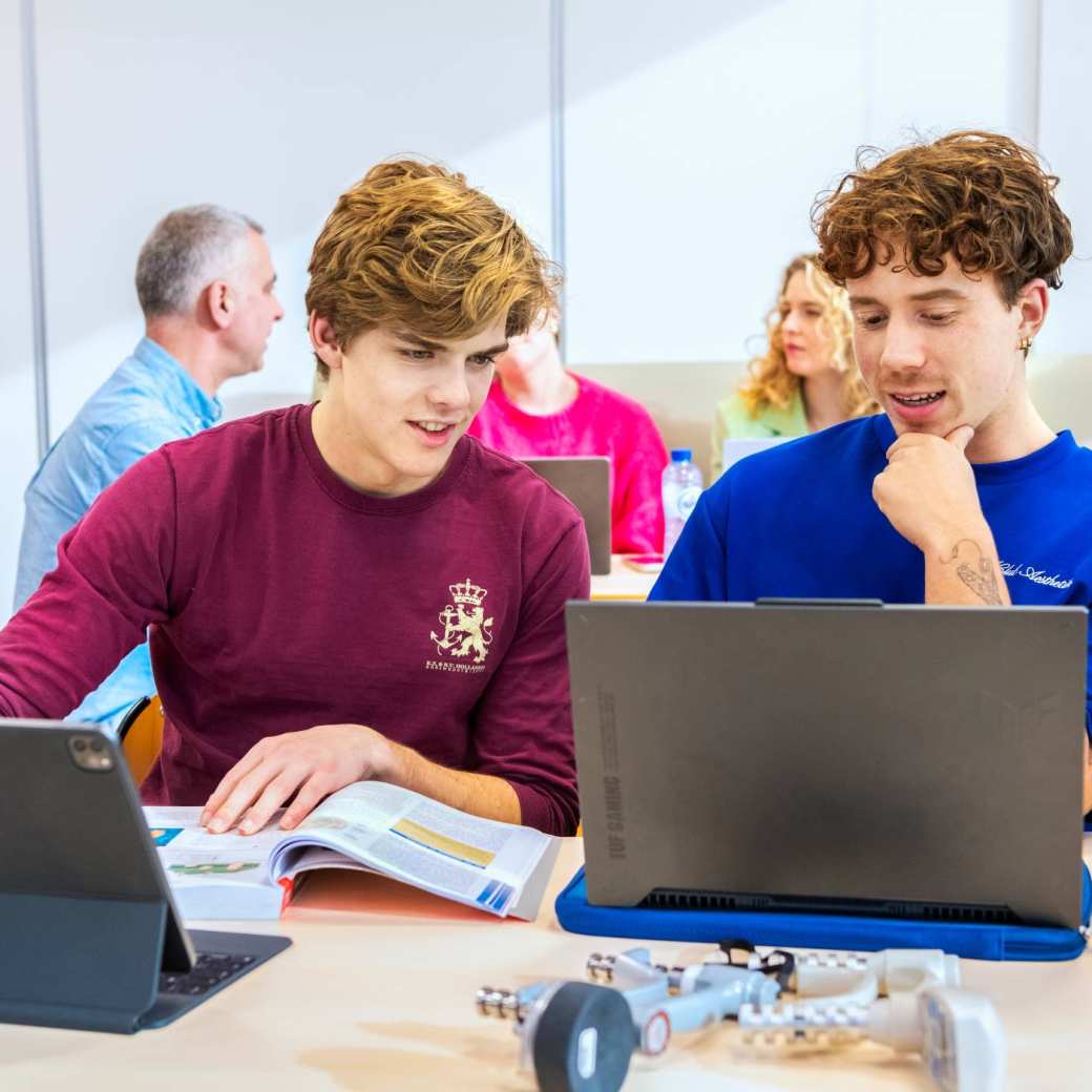 2 zij-instromers overleggen met een boek en 2 laptops.