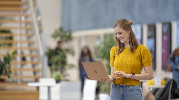 Student staat in een hal kijkend op haar laptop