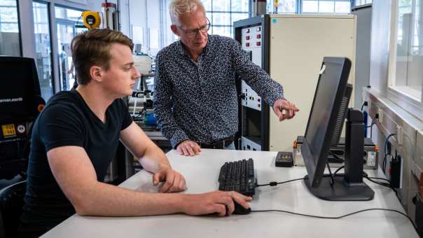 Een automotive docent kijkt met een student mee op de computer.