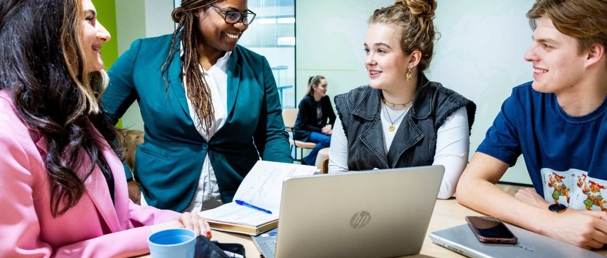 Studenten Human Resource Management (HRM) in gesprek met een docent met een laptop erbij