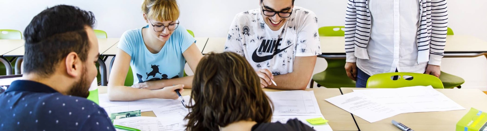 studenten werken aan tafel en docent kijkt mee