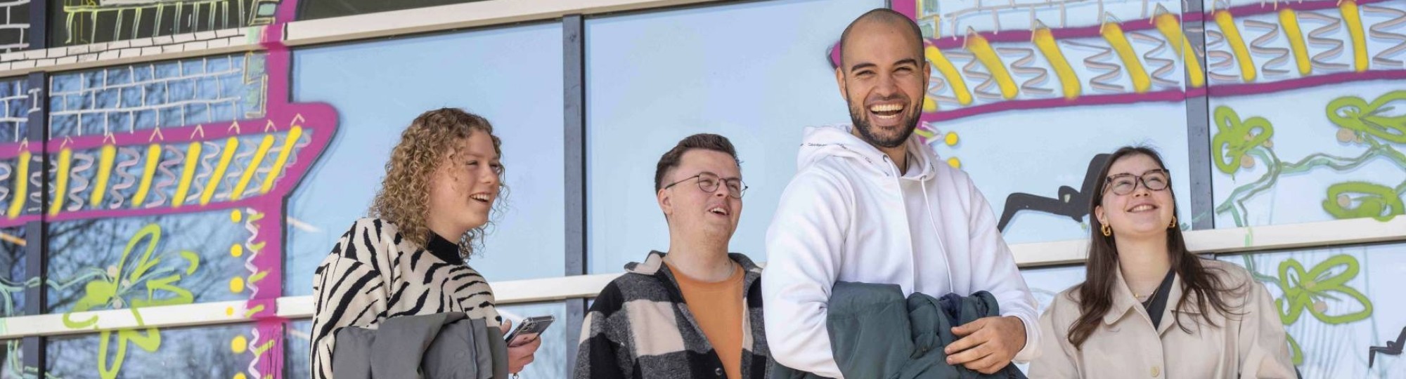 Groep student en een docent lachend voor een vrolijke wand