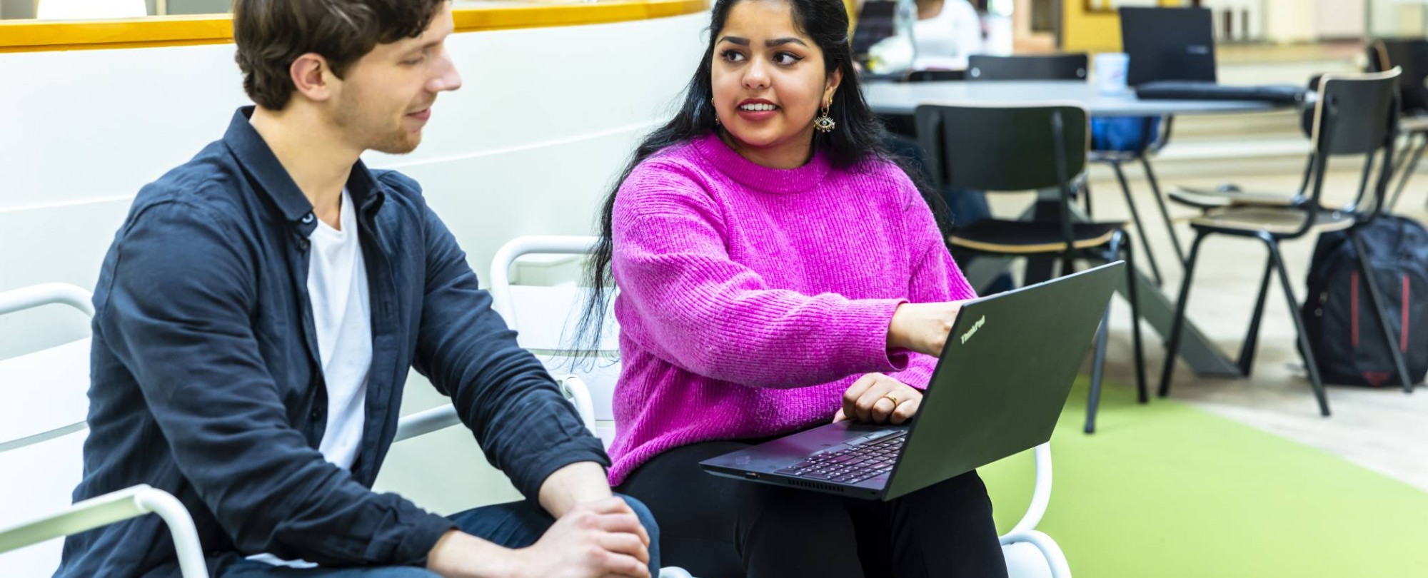 twee studenten hbo-ict zijn in gesprek terwijl een van hen een laptop op schoot heeft