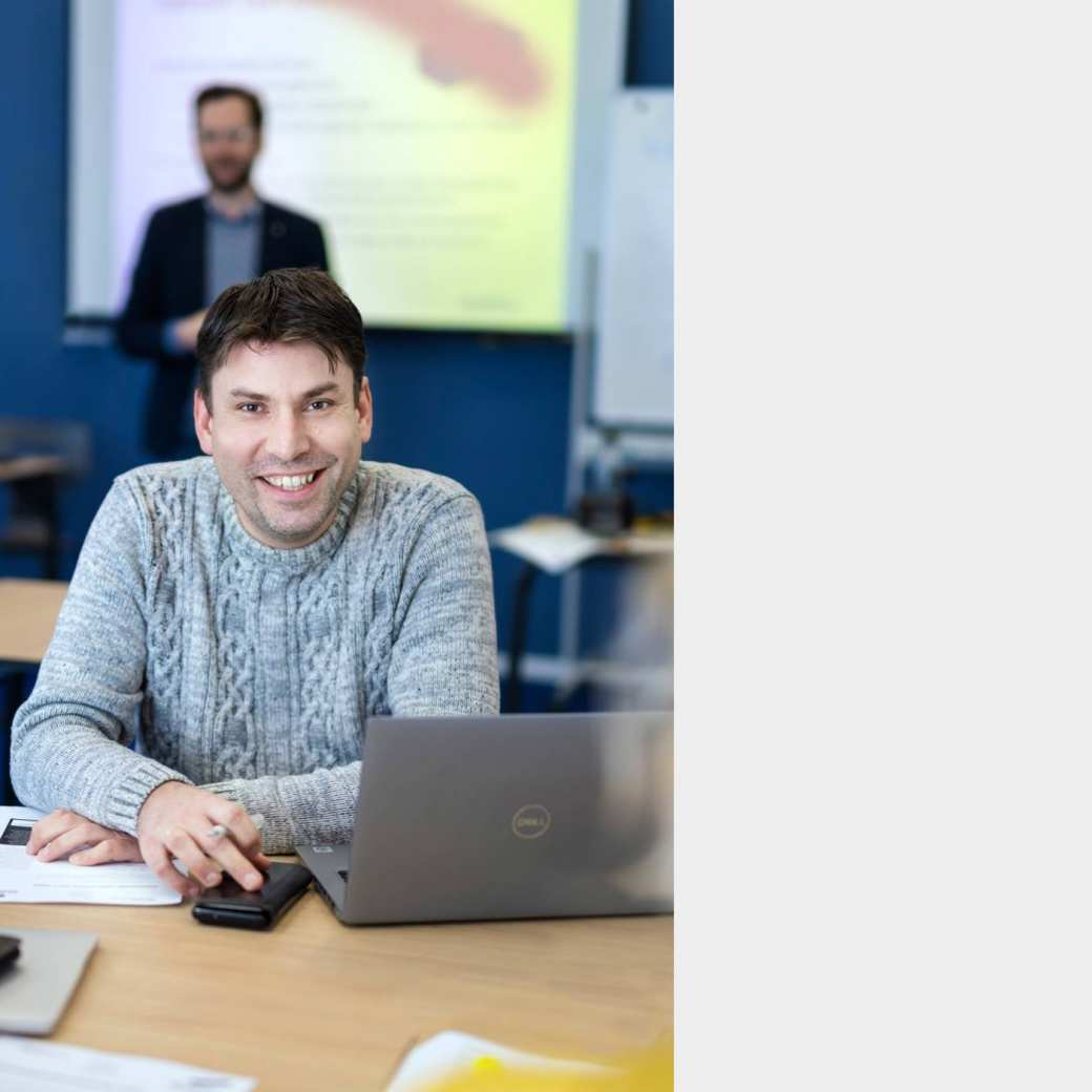 ALLEEN VOOR DE MANP | Een masterstudent met laptop bij een les onderzoek met op de achtergrond een docent van de Master Advanced Nursing Practice.