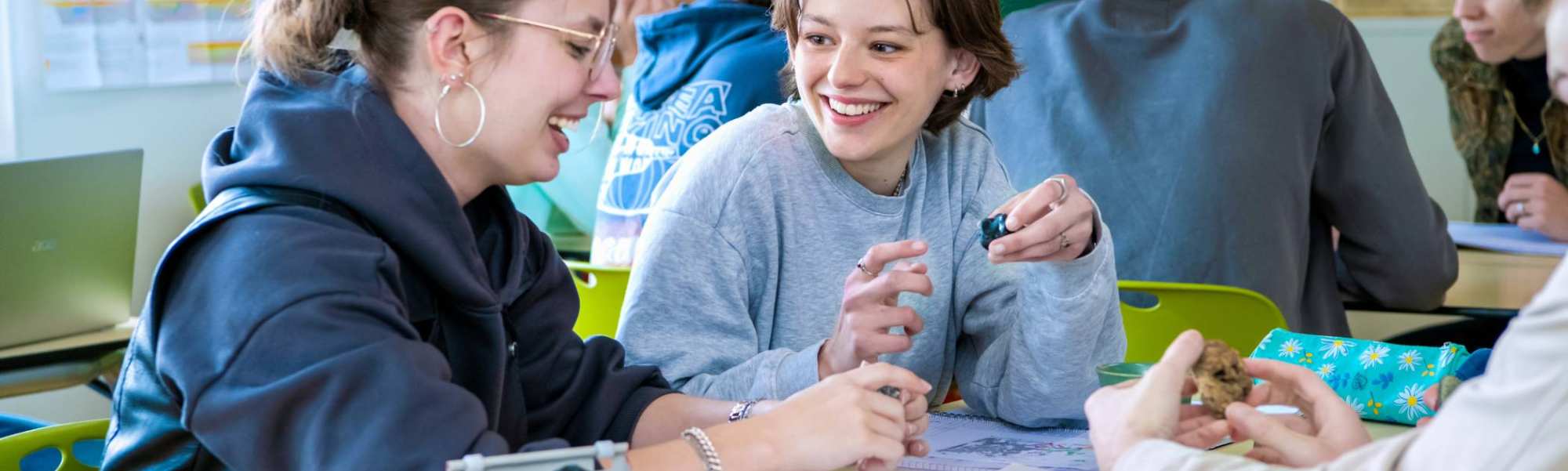 Twee studenten lachen naar elkaar in de klas. 