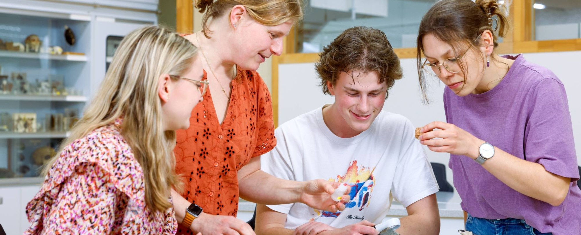 Eén docent en drie studenten onderzoeken samen stenen in het lab.