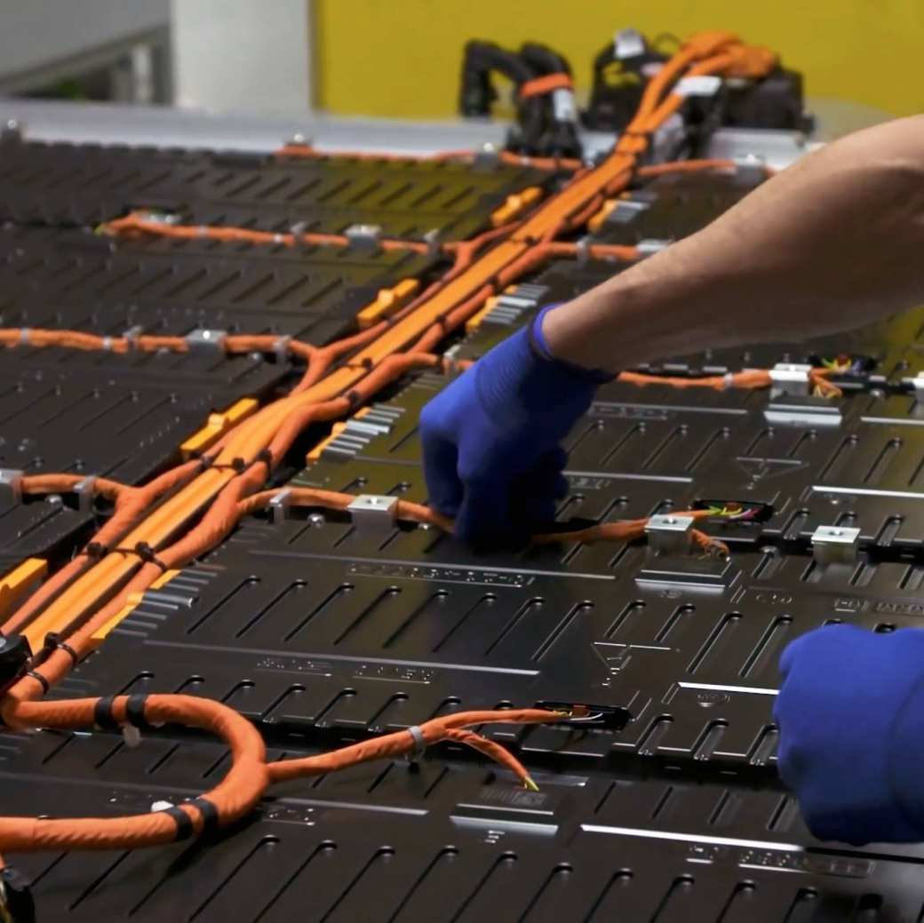 Monteur met grijze handschoenen aan de slag met een batterij met oranje draden. Seece - SEE- elektrotechniek, werktuigbouwkunde