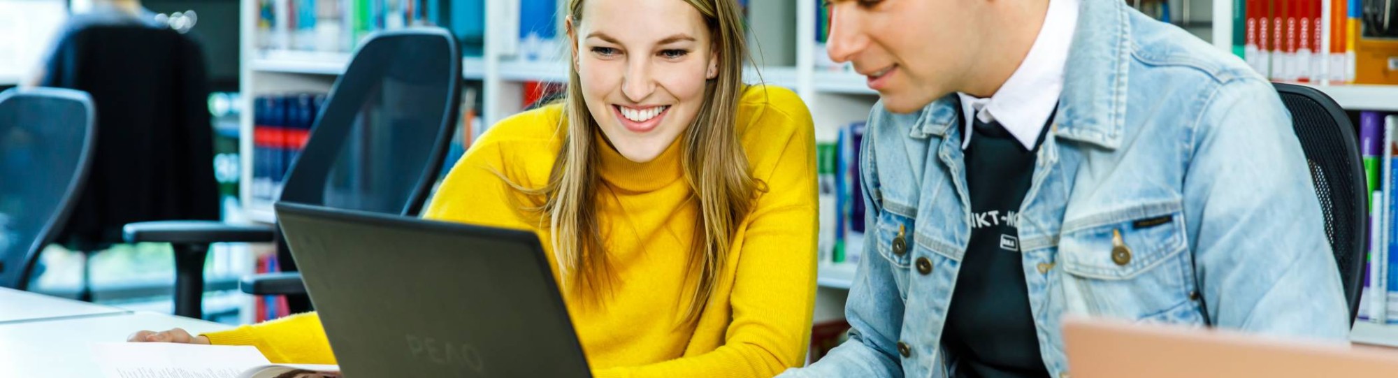 Twee HAN-studenten Leraar Nederlands werken achter één laptop in de mediatheek. 