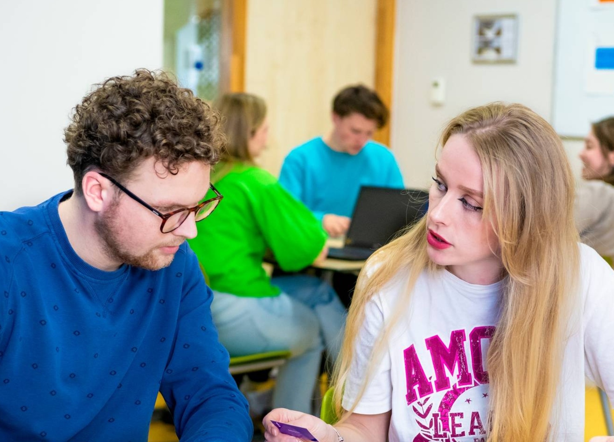 Twee studenten spelen een kaartspel met blauwe kaartjes in een gekleurd leraar Duits lokaal.
