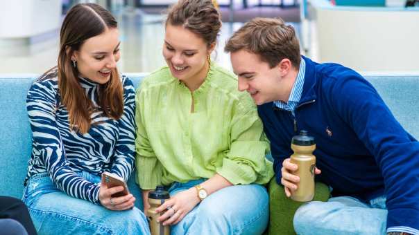 Studenten lachen en kijken naar een telefoon.