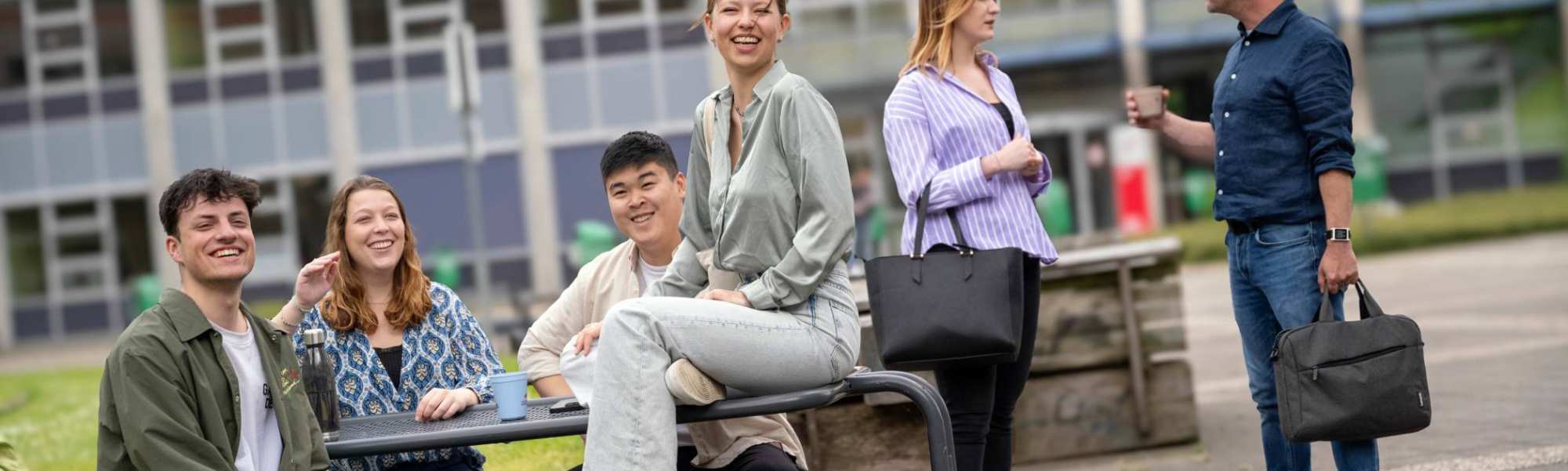 Groepje studenten zitten buiten aan de picknicktafel, op de campus Arnhem, kijken in de camera. 