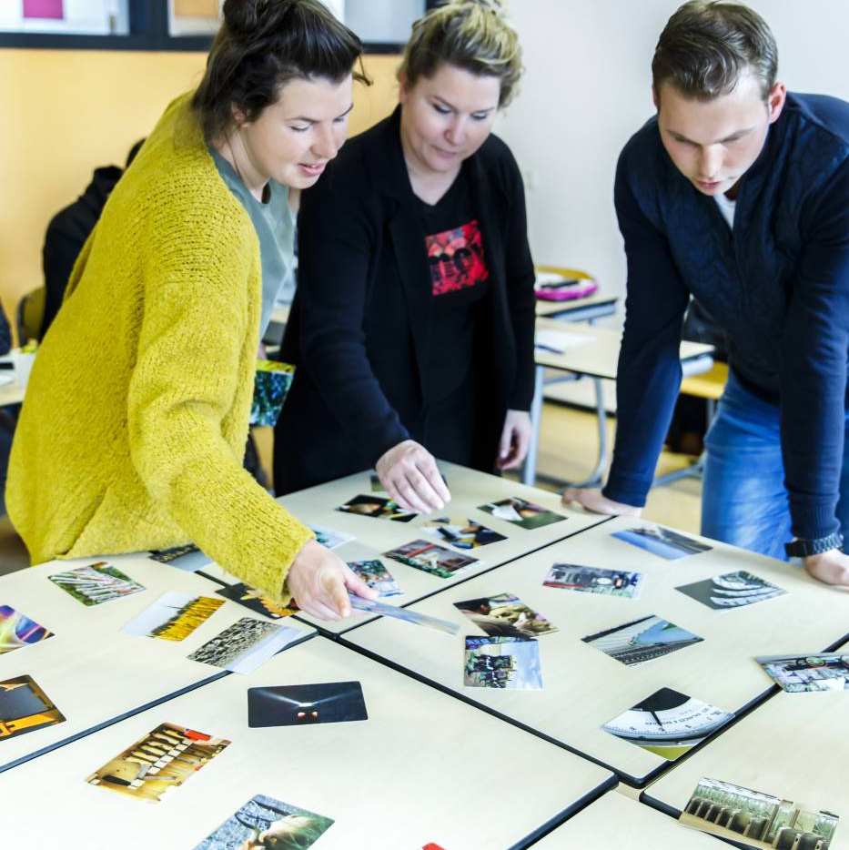 drie mensen kijken naar fotos op tafel