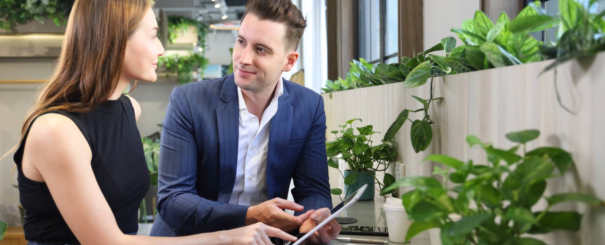 Foto van twee mensen in overleg met een tablet in kantoorruimte met planten voor projectpagina van het ass. lectoraat Sustianable Finance & Tax.