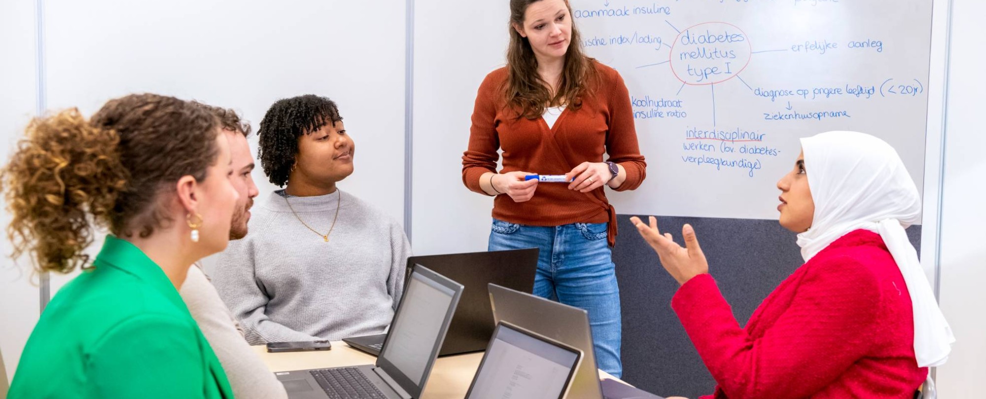 Docent staat voor een whiteboard en luistert naar een vraag van een leerling over diabetes.