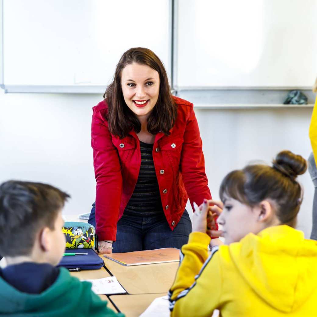 Docent luistert naar haar drie studenten die aan de tafel zitten te overleggen.