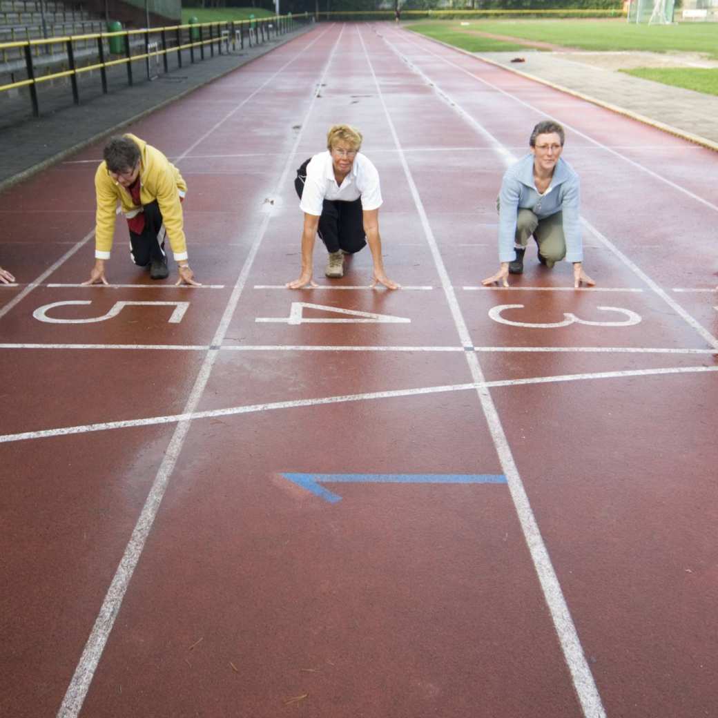 Een groepje actieve ouderen in de starthouding bij de startlijn van een hardloopbaan.