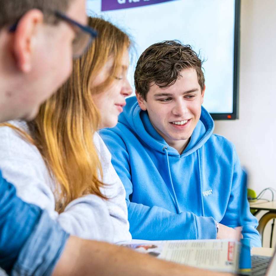 Twee studenten kijken naar wat hun medestudent aanwijst op het A4'tje.