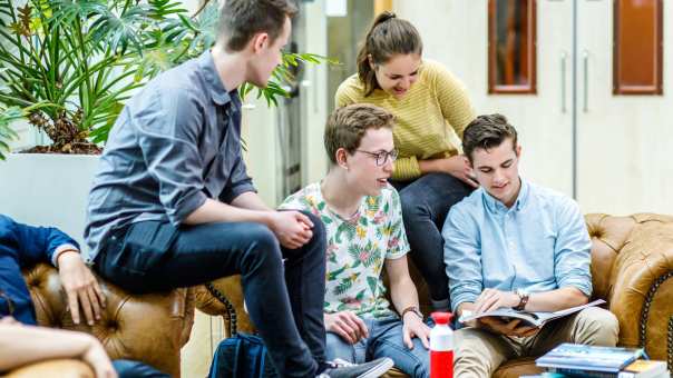 Vier studenten van Leraar Aardrijkskunde zitten op de bank en bladeren door de atlas. 