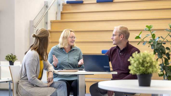 3 studenten in gesprek aan tafel met een laptop.