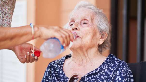 Een oude vrouw drinkt uit een flesje.