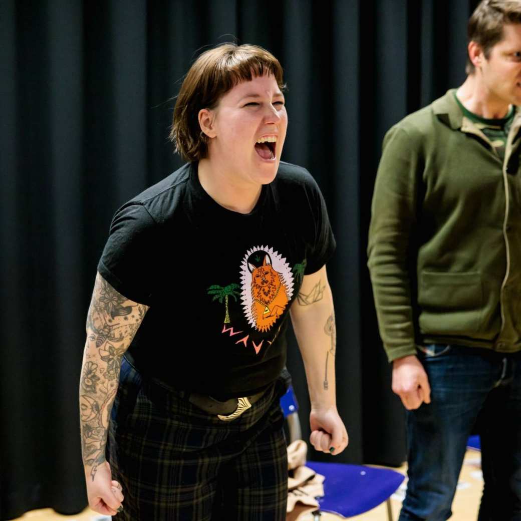 Vrouw in zwart shirt met tatoeages aan het schreeuwen met ander schreeuwend persoon op de achtergrond