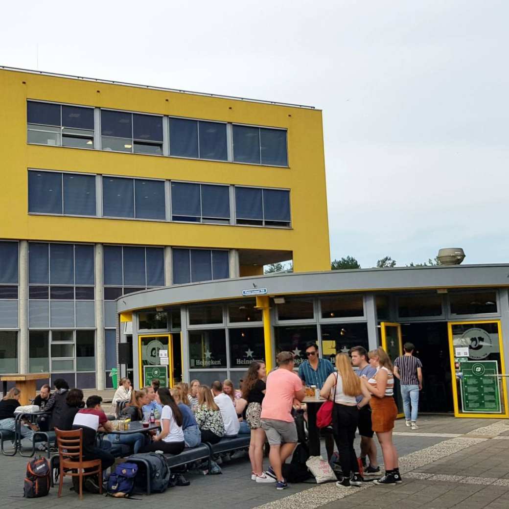 Studenten komen na de lessen samen bij Lokaal 99 om iets te drinken. Op de achtergrond het onderwijsgebouw van Engineering en Automotive.