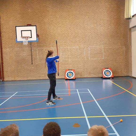 Docent Leontien Thewissen in de gymzaal met pijl en boog. 