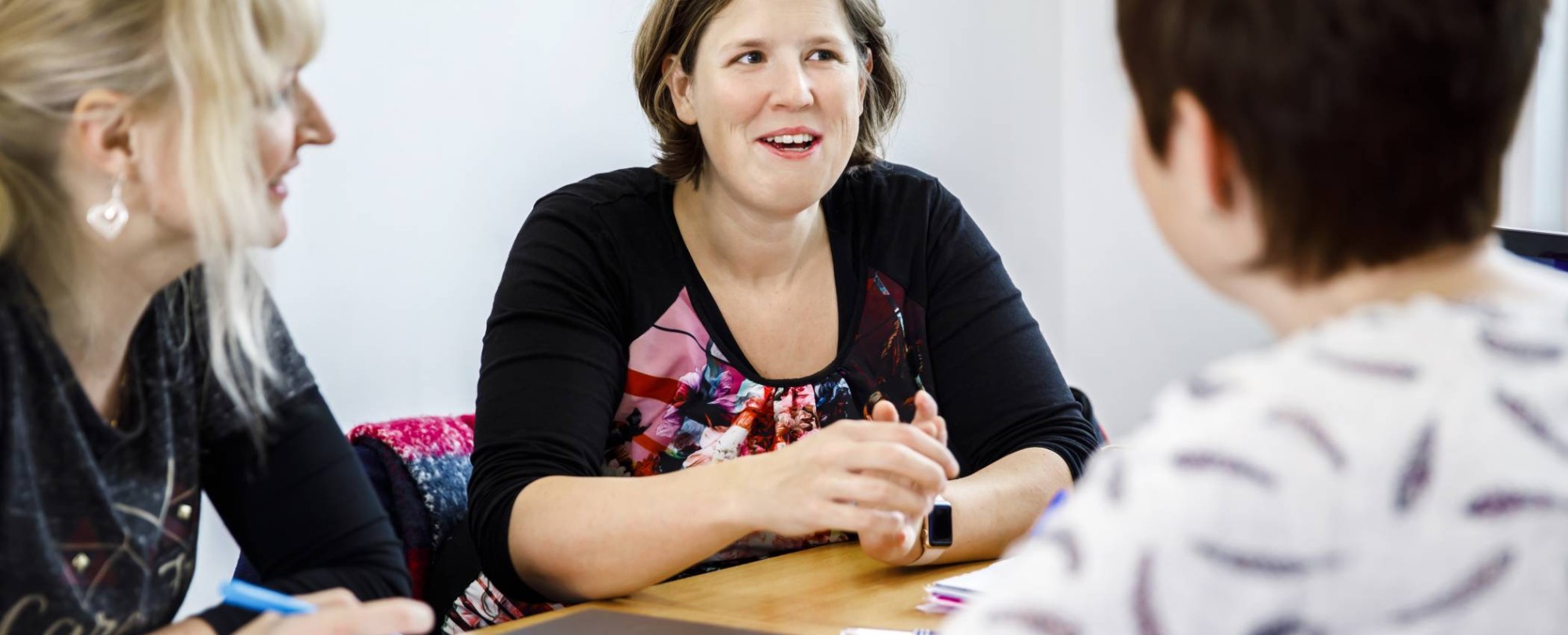 Drie vrouwen zijn aan het overleggen en een van de vrouwen schrijft in een notitieboek