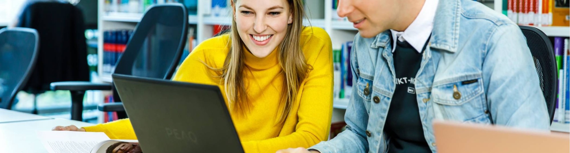 Twee HAN-studenten Leraar Nederlands werken achter één laptop in de mediatheek. 