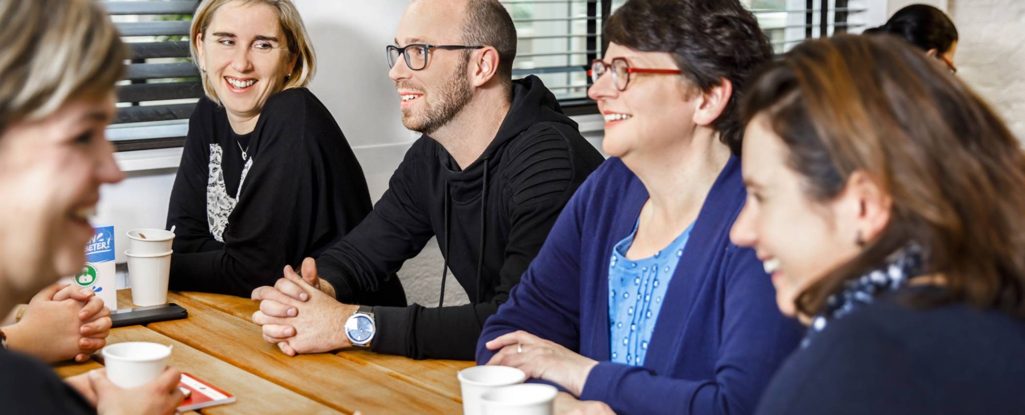 Vijf studenten die aan het overleggen zijn aan een houten tafel