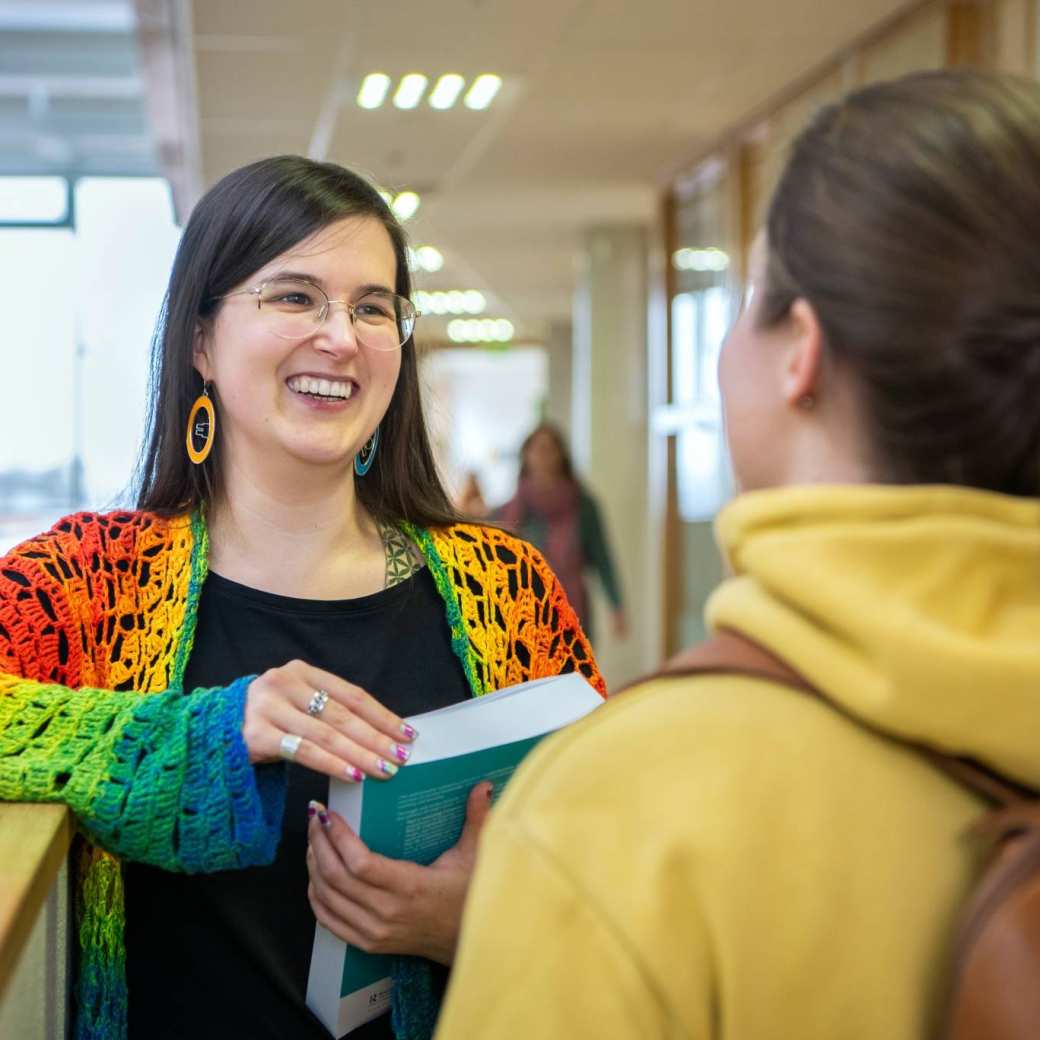 Foto Master Academie Educatie. 2 masterstudenten staan in de gang op Kapittelweg 35 in Nijmegen te praten, 1 met een boek in de hand.