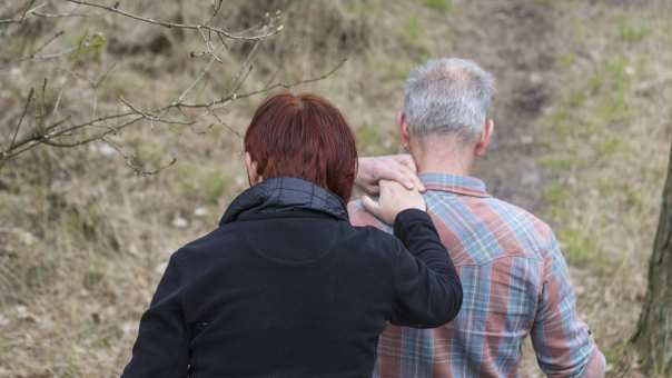 Vrouw steunt man tijdens wandeling in het bos. Sneller Herstel. Helpende hand.