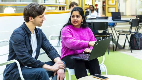 twee studenten hbo-ict zijn in gesprek terwijl een van hen een laptop op schoot heeft