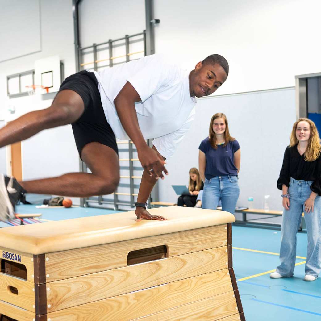 Student Psychomotorische therapie springt over een obstakel in een gymlokaal tijdens een praktijkles