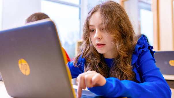 Groep 5,6,7 op de school Da Vince. Een leerling is aan het werk achter haar laptop in de klas. 