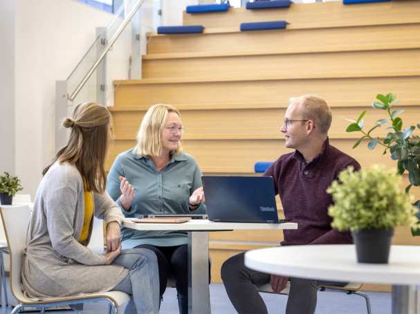 3 studenten in gesprek aan tafel met een laptop.