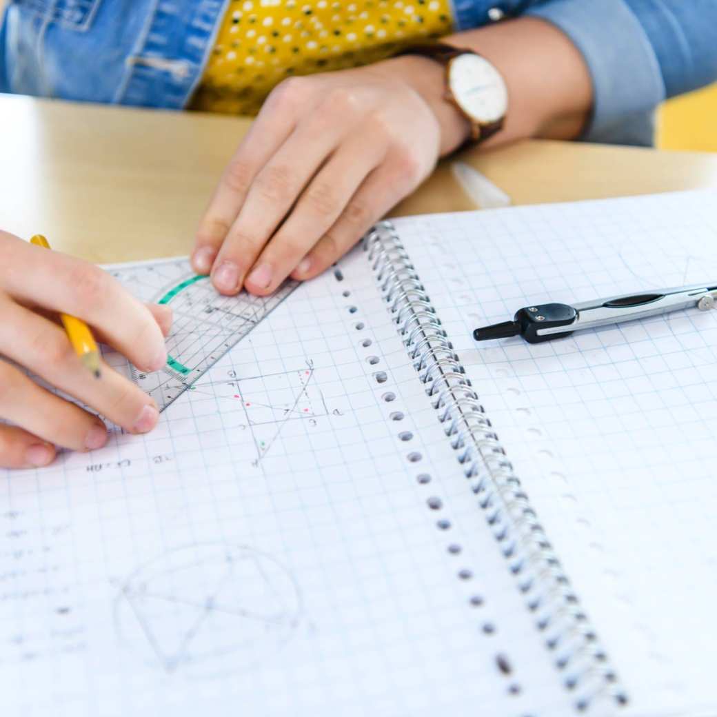 Handen boven schrift met een geodriehoek.